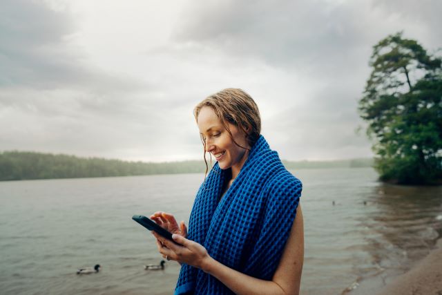 A woman standing on a beach with her phone i her hand SMALL